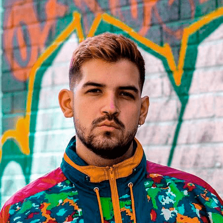 A young man with padlock beard standing in front of a graffiti covered wall